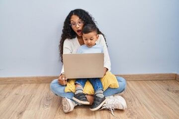 Sticker - Young hispanic mother and kid using computer laptop sitting on the floor in shock face, looking skeptical and sarcastic, surprised with open mouth