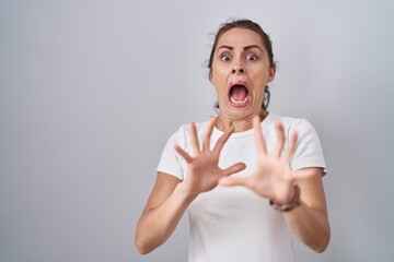 Sticker - Beautiful brunette woman standing over isolated background afraid and terrified with fear expression stop gesture with hands, shouting in shock. panic concept.