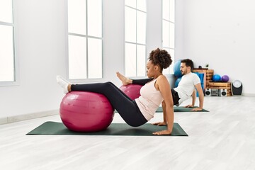 Young african american woman and hispanic man exercising at pilates room, stretching body and doing yoga pose, training strength and balance