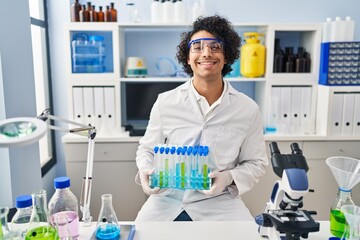 Sticker - Hispanic man with curly hair working at scientist laboratory looking positive and happy standing and smiling with a confident smile showing teeth