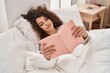 © Krakenimages.com - Young hispanic woman reading book lying on bed at bedroom