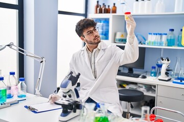 Wall Mural - Young hispanic man scientist writing on document holding urine test tube at laboratory