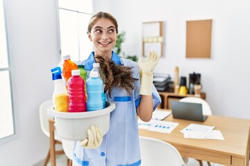 Canvas Print - Young blonde woman wearing cleaner uniform holding cleaning products smiling cheerful presenting and pointing with palm of hand looking at the camera.