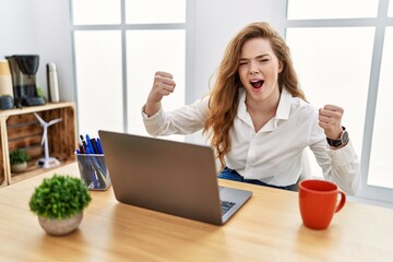 Sticker - Young caucasian woman working at the office using computer laptop angry and mad raising fists frustrated and furious while shouting with anger. rage and aggressive concept.