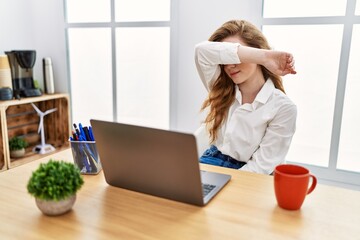 Poster - Young caucasian woman working at the office using computer laptop covering eyes with arm, looking serious and sad. sightless, hiding and rejection concept