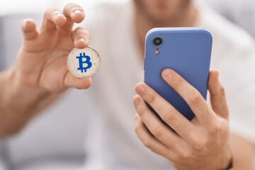 Canvas Print - Young caucasian man using smartphone holding bitcoin at home