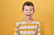 Young caucasian kid standing over yellow background sticking tongue out happy with funny expression. emotion concept.