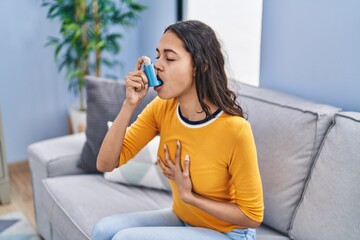 Poster - Young african american woman using inhaler sitting on sofa at home