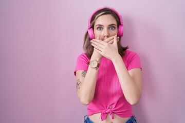 Canvas Print - Blonde caucasian woman listening to music using headphones shocked covering mouth with hands for mistake. secret concept.