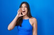 © Krakenimages.com - Hispanic woman standing over blue background shouting and screaming loud to side with hand on mouth. communication concept.