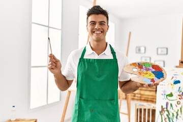 Sticker - Young hispanic man smiling confident holding paintbrush and palette at art studio