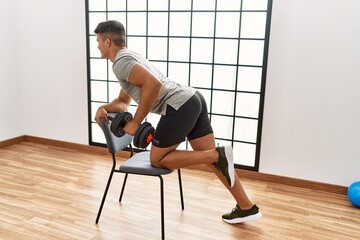 Young hispanic man training using dumbbells at sport center