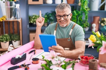 Wall Mural - Hispanic man with grey hair working at florist shop doing video call with tablet smiling with an idea or question pointing finger with happy face, number one