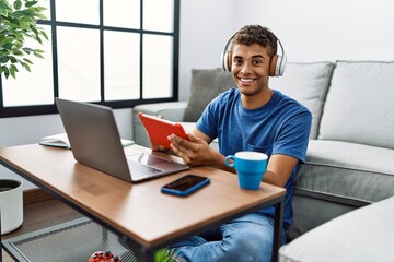 Poster - Young hispanic man using laptop and touchpad device at home