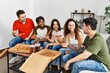 © Krakenimages.com - Group of young friends smiling happy eating italian pizza sitting on the sofa at home.