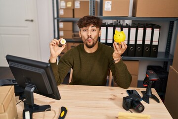 Canvas Print - Arab man with beard working at small business ecommerce holding bitcoin making fish face with mouth and squinting eyes, crazy and comical.