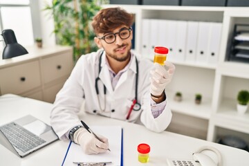 Sticker - Young arab man wearing doctor uniform writing on document analysing urine test tube at clinic