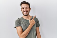 Young Hispanic Man With Beard Wearing Casual T Shirt Over White Background Cheerful With A Smile Of Face Pointing With Hand And Finger Up To The Side With Happy And Natural Expression On Face