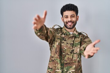 Poster - Arab man wearing camouflage army uniform looking at the camera smiling with open arms for hug. cheerful expression embracing happiness.