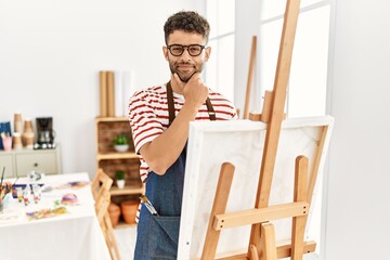 Canvas Print - Arab young man at art studio looking confident at the camera smiling with crossed arms and hand raised on chin. thinking positive.