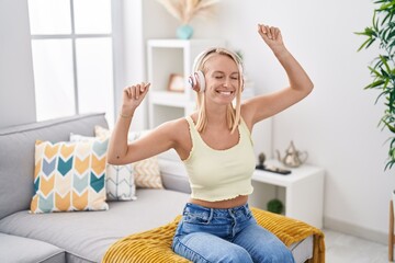 Poster - Young blonde woman listening to music sitting on sofa at home