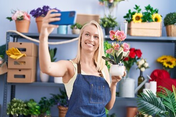 Wall Mural - Young blonde woman florist make selfie by smartphone holding plant at florist store