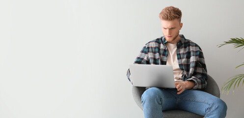 Canvas Print - Handsome student with laptop sitting on chair against light background with space for text