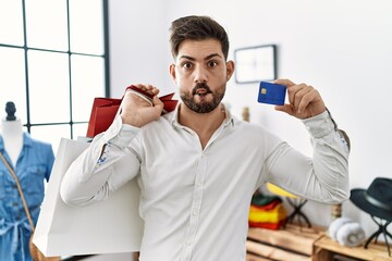 Sticker - Young man with beard at retail shop holding shopping bags and credit card making fish face with mouth and squinting eyes, crazy and comical.