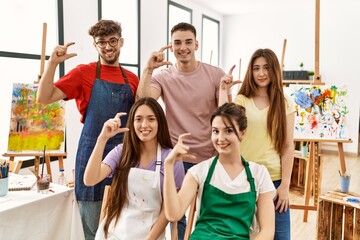 Canvas Print - Group of five hispanic artists at art studio smiling and confident gesturing with hand doing small size sign with fingers looking and the camera. measure concept.