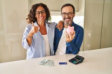 Middle Age Couple Holding Piggy Bank Calculating Savings Smiling Happy And Positive, Thumb Up Doing Excellent And Approval Sign