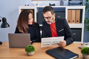 Wall Mural - Middle age man and woman business workers using laptop reading document at office