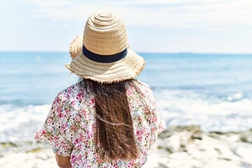 Poster - Young latin girl on back view wearing summer hat sitting on the bench at the beach.