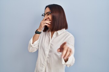 Sticker - Young hispanic woman standing over white background laughing at you, pointing finger to the camera with hand over body, shame expression