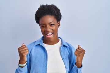 Poster - African american woman standing over blue background celebrating surprised and amazed for success with arms raised and eyes closed. winner concept.