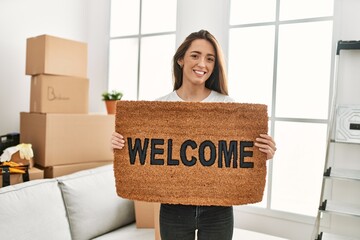 Young hispanic woman smiling confident holding welcome doormat at new home