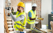 © JackF - Working process at indoor building site, one skilled maintenance worker working with hammer drill perforator, another one carrying wooden construction materials