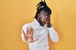 © Krakenimages.com - African man with dreadlocks wearing turtleneck sweater over yellow background covering eyes with hands and doing stop gesture with sad and fear expression. embarrassed and negative concept.