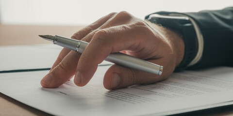 Wall Mural - Male hand holding a pen resting on a business contract