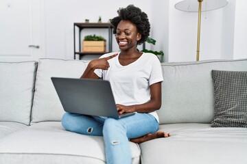 Sticker - African young woman using laptop at home smiling happy pointing with hand and finger