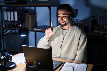 Canvas Print - Young handsome man working using computer laptop at night showing and pointing up with finger number one while smiling confident and happy.