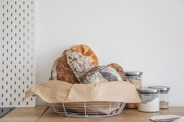 Canvas Print - Basket with loaves of fresh bread, parchment paper and jars on kitchen counter near light wall