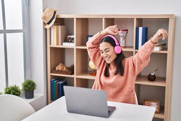 Wall Mural - Young hispanic woman listening to music and dancing sitting on table at home