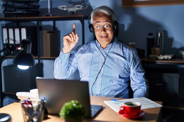 Wall Mural - Hispanic senior man wearing call center agent headset at night pointing finger up with successful idea. exited and happy. number one.