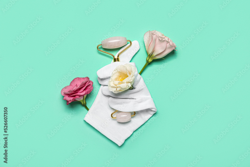 Facial massage tool with glove and flowers on green background