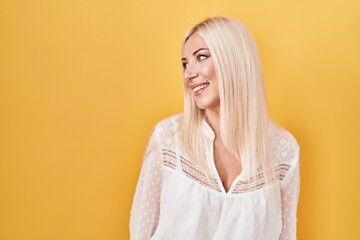 Poster - Caucasian woman standing over yellow background looking away to side with smile on face, natural expression. laughing confident.