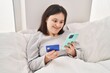 © Krakenimages.com - Young woman with down syndrome using smartphone and credit card sitting on bed at bedroom