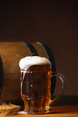 Mug of fresh beer with spikelets and barrel on table against dark background. Oktoberfest celebration