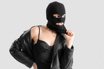 Young woman in balaclava and leather jacket looking aside on light background