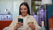 © Andrii Iemelianenko - Lovely girl using credit bank card and smartphone while transferring money, purchases online shopping, order food delivery at modern home apartment indoors. Young woman in living room lying on couch