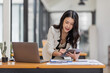 © David - Female Business Asian working on documents on tablet laptop in the workplace, Young asian woman sitting at table doing planning financial report, business plan investment, finance analysis concept.